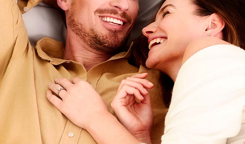 Couple lying relaxed with woman wearing emerald cut lab grown diamond engagement ring on hand