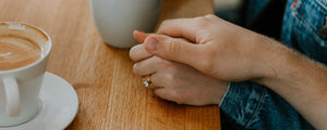 Couple holding hands woman wearing yellow gold oval engagement ring at coffee shop