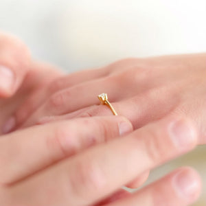 man sliding dainty engagement ring on woman's hand