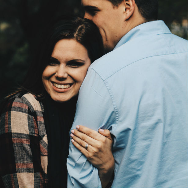 smiling woman holding man's arm while wearing engagement ring