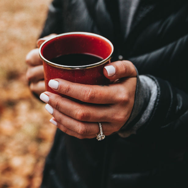 woman's hands holding coffee cup wearing trellis engagement ring