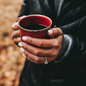 woman's hands holding coffee cup wearing trellis engagement ring